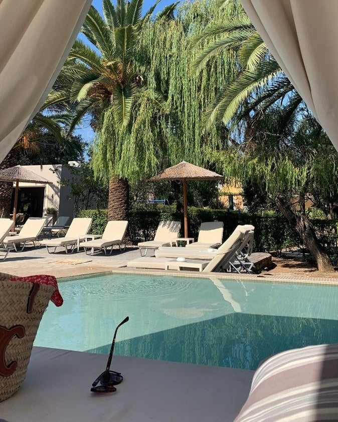 A serene poolside scene viewed from a shaded cabana, framed by flowing white curtains.